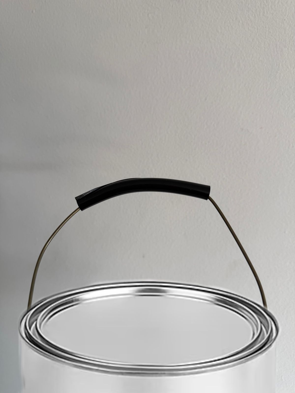 A metal paint can with its lid on, photographed from slightly above against a plain light-grey wall. A black Safety Grip is fitted over the top of the can's thin wire handle.